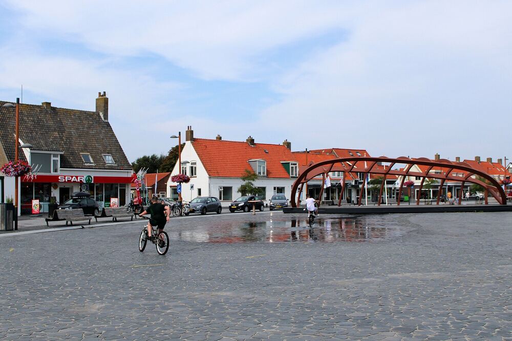 Het dorpsplein van Petten met rode boogconstructie, witte huizen met rode daken en een fietser